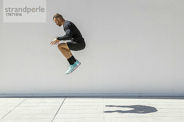 Männlicher Athlet springt an einem sonnigen Tag an der Wand entlang