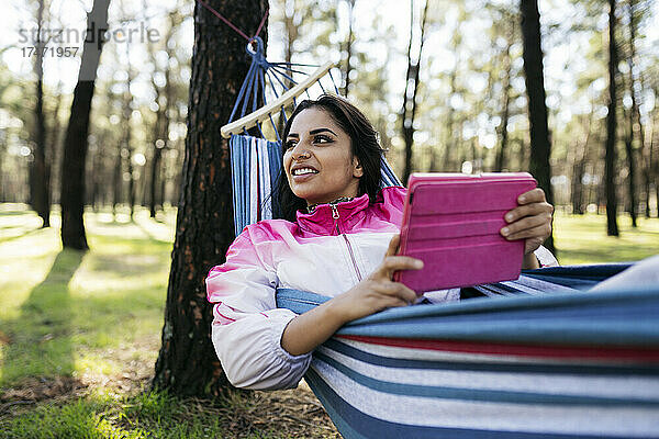 Junge Frau hält digitales Tablet in Hängematte im Park