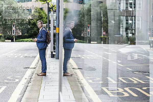 Junger Geschäftsmann mit Rucksack wartet an Bushaltestelle