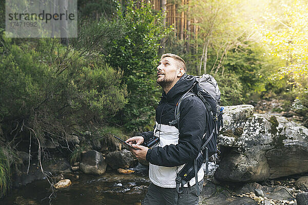 Männlicher Tourist mit digitalem Tablet blickt im Wald nach oben