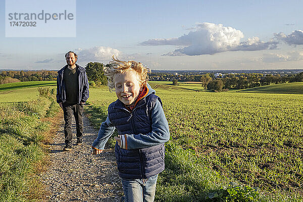 Fröhlicher Junge läuft vor seinem Vater auf dem Feld