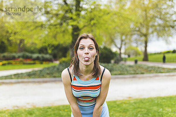 Verspielte Frau streckt im öffentlichen Park die Zunge heraus