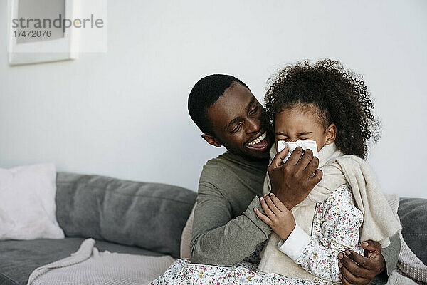 Glücklicher Vater wischt Tochter zu Hause mit Taschentuch die Nase ab