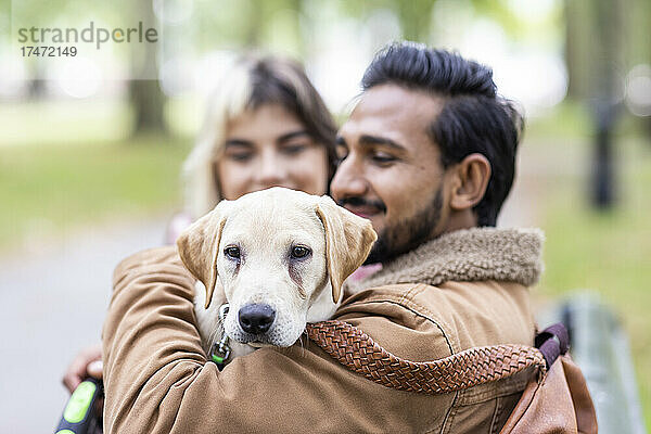 Lächelnder junger Mann mit Hund im öffentlichen Park