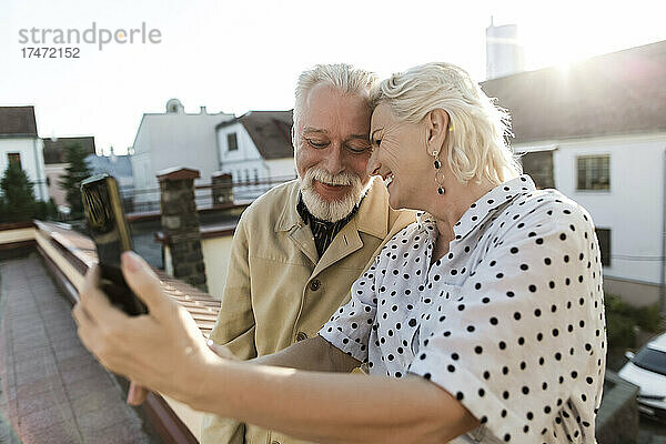 Lächelnde Frau macht Selfie mit Mann per Smartphone auf der Terrasse