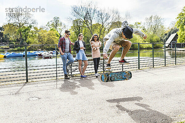 Freunde schauen Mann zu  der im Park Stunt auf Skateboard übt