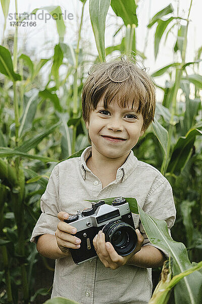 Lächelnder Junge hält Kamera im Maisfeld