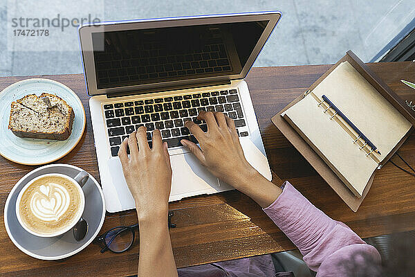 Geschäftsfrau mit Kaffeetasse und Gebäck mit Laptop am Cafétisch