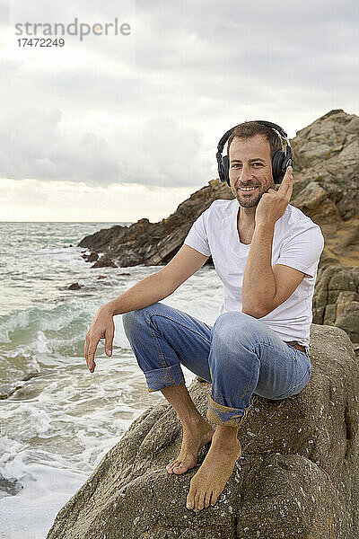 Lächelnder Mann  der am Strand Musik über Kopfhörer hört