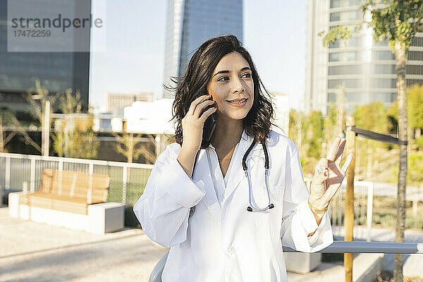 Lächelnde Ärztin  die vor dem Gebäude mit dem Smartphone spricht
