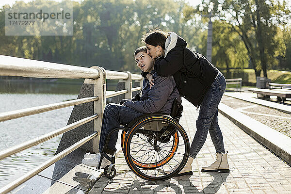 Freundin küsst Freund  der im Rollstuhl am Ufer sitzt