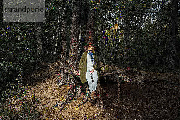 Frau mittleren Alters sitzt am Baumstamm im Wald