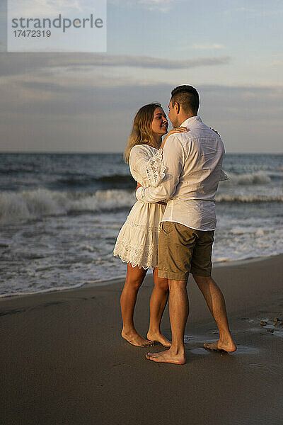 Junges Paar schaut einander an  während es bei Sonnenuntergang am Strand steht