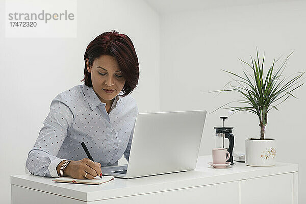 Geschäftsfrau schreibt im Notizblock  während sie im Heimbüro arbeitet
