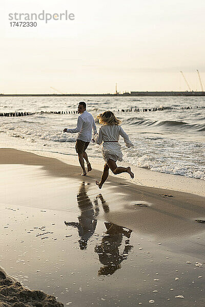 Junges Paar läuft bei Sonnenuntergang am Strand
