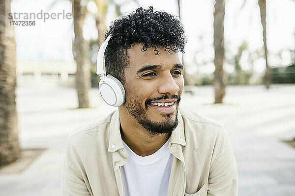Lächelnder junger Mann  der über kabellose Kopfhörer Musik hört