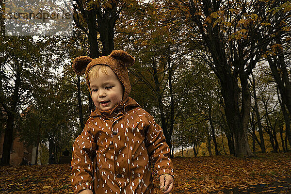 Kleinkind mit brauner Mütze und Regenmantel im Herbstpark
