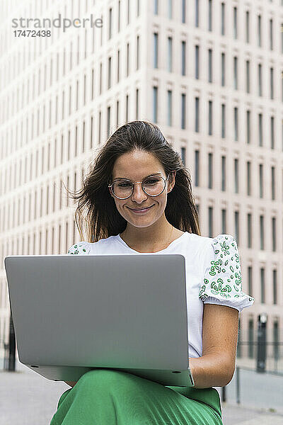 Lächelnde junge Geschäftsfrau  die in der Stadt am Laptop arbeitet