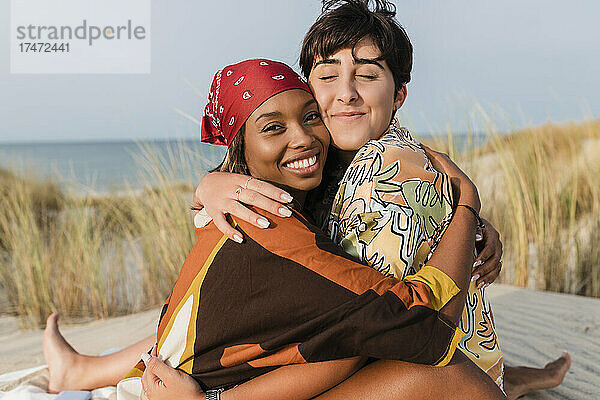 Lächelnde lesbische Frauen umarmen sich am Strand
