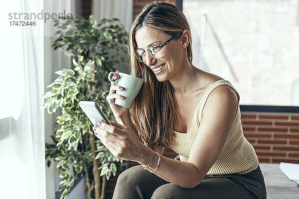Lächelnde Geschäftsfrau benutzt Mobiltelefon  während sie am Schreibtisch sitzt