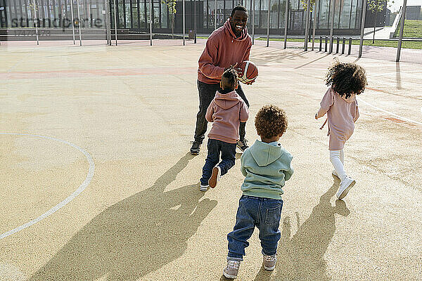 Fröhlicher Vater spielt Basketball mit Kindern auf dem Sportplatz