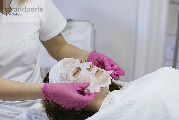 Kosmetikerin trägt Frau im Salon feuchtigkeitsspendende Gesichtsmaske auf