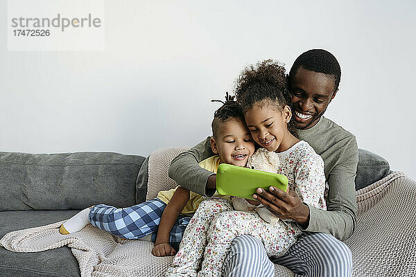 Lächelnder Mann mit Sohn und Tochter  die ein digitales Tablet auf dem Sofa nutzen