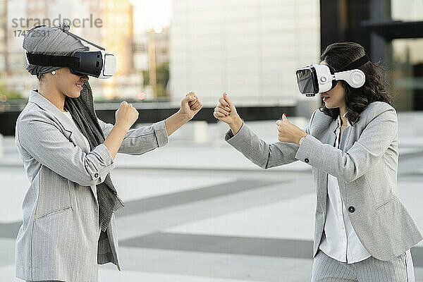 Junge Geschäftsfrau spielt mit einer Kollegin  während sie einen Virtual-Reality-Simulator trägt