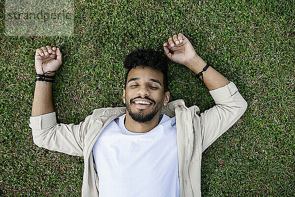 Happy young man with eyes closed relaxing on grass