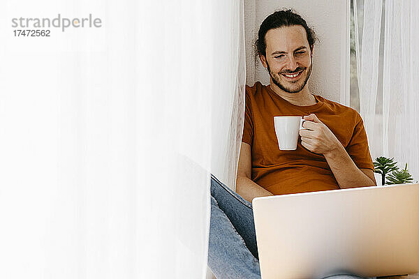Mann trinkt Kaffee  während er zu Hause arbeitet