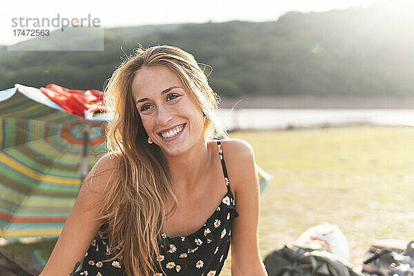 Schöne junge Frau lächelt an einem sonnigen Tag am Seeufer
