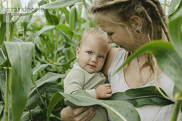 Mutter trägt Kleinkind im Maisfeld