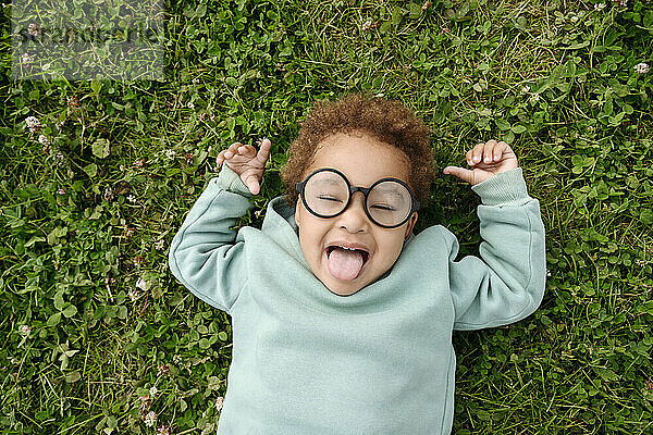 Süßes Mädchen mit Brille  das die Zunge auf dem Gras herausstreckt