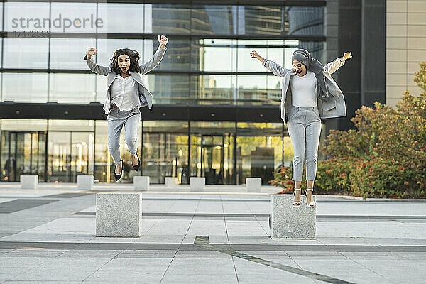 Fröhliche Kolleginnen springen auf dem Fußweg vor dem Gebäude