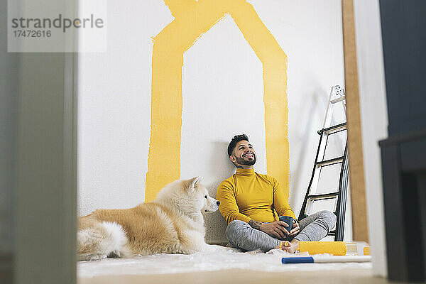 Lächelnder Mann sitzt mit gekreuzten Beinen vor Hund zu Hause