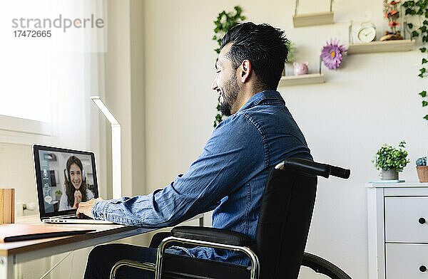Lächelnder Geschäftsmann  der zu Hause mit einer Geschäftsfrau über eine Videokonferenz über einen Laptop spricht