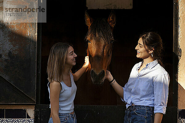 Lächelnde Freunde reden und streicheln Pferd im Stall