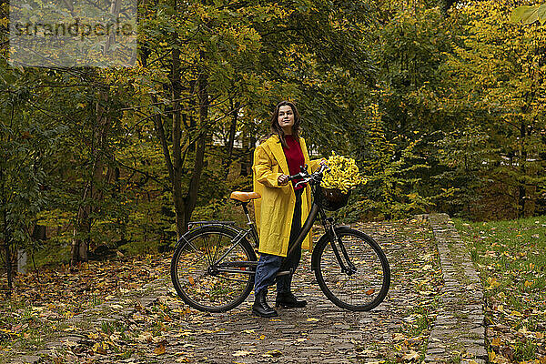Frau im Regenmantel steht mit Blumen im Fahrradkorb