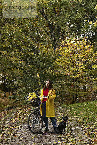 Frau steht mit Fahrrad und Hund im öffentlichen Park