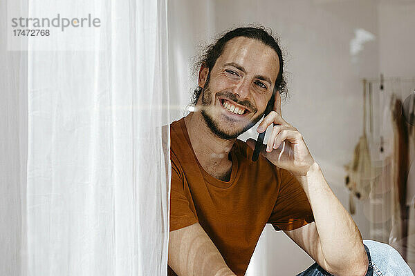 Lächelnder Mann  der mit dem Handy spricht und aus dem Fenster schaut