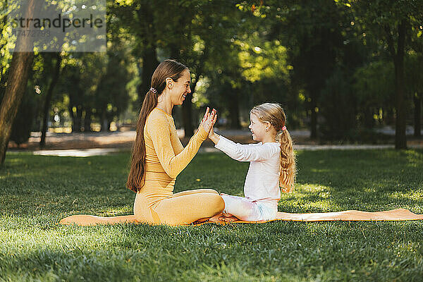 Lächelnde Tochter berührt die Hände der Mutter auf der Trainingsmatte im Park