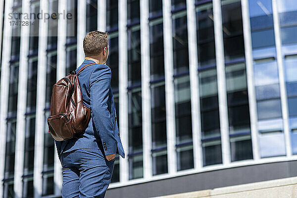 Geschäftsmann mit der Hand in der Tasche blickt an einem sonnigen Tag auf das Gebäude