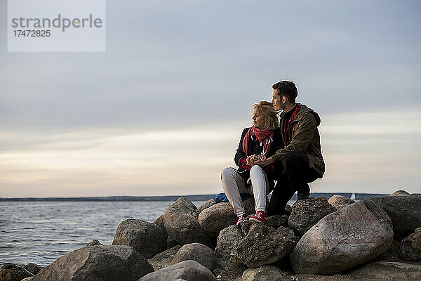 Paar blickt aufs Meer  während es auf einem Felsen sitzt