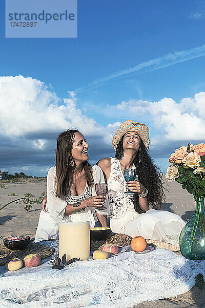 Freundinnen mit Getränken genießen Picknick am Strand