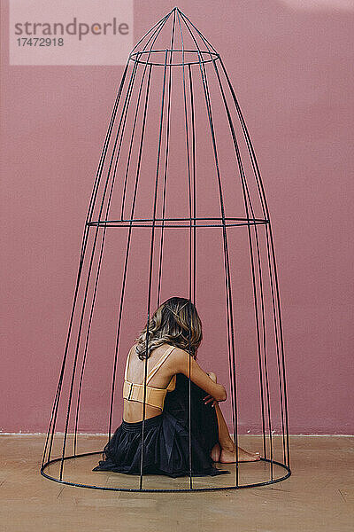 Frau mit braunen Haaren umarmt Knie  während sie im Käfig sitzt