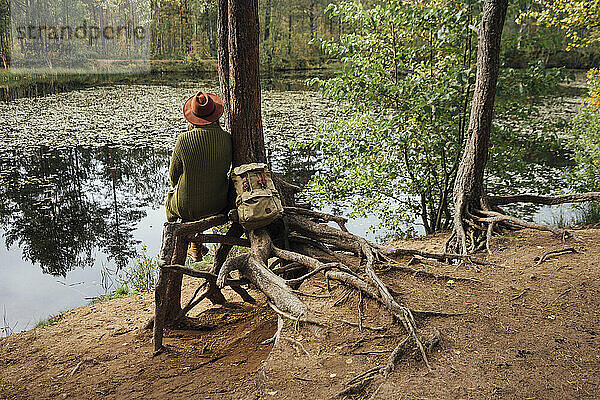 Frau blickt auf den See  während sie neben einem Baum im Wald sitzt