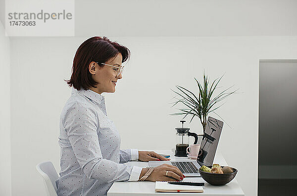 Lächelnder Freiberufler  der vom Heimbüro aus am Laptop arbeitet