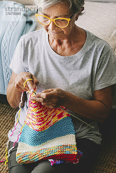 Ältere Frau strickt Wolle mit Nadel im Wohnzimmer