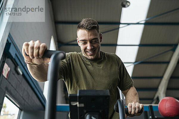 Lächelnder männlicher Athlet  der im Fitnessstudio auf dem Crosstrainer trainiert