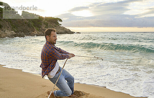 Mann zieht am Strand Seil aus dem Meer